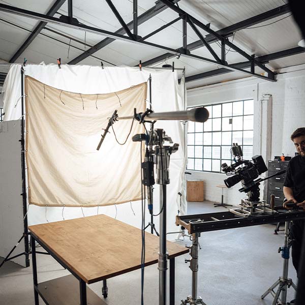 Ein Filmset mit professionellen Kameras, Mikrofonen und Beleuchtungsanlagen auf einem Holztisch, während ein Crewmitglied die Ausrüstung in einem geräumigen Studio der Filmproduktion Saarbrücken mit großen Fenstern einstellt.